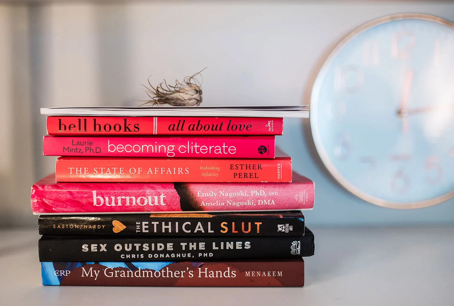 A stack of books in Dr. Lily's office including All About Love, Becoming Cliterate, and My Grandmother's Hands
