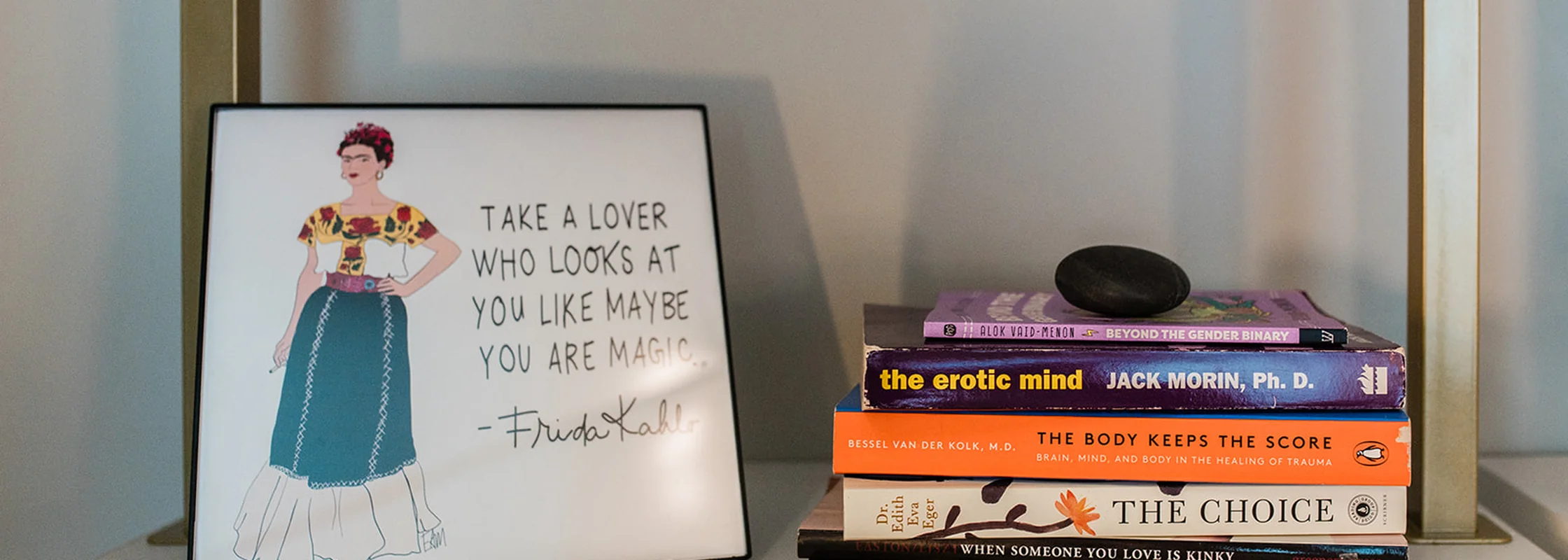 A framed Frida Kahlo print and a stack of books on the shelf in Dr. Lily Zehner's office